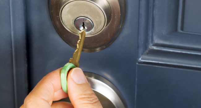 Photo of female hand putting house key into front door lock of house